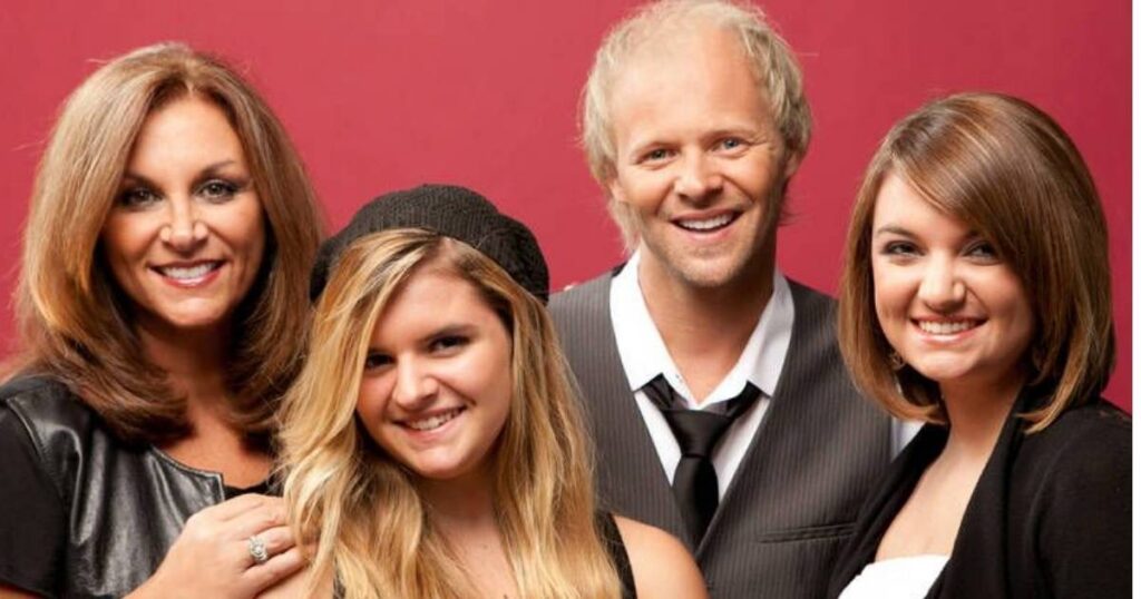 Four people posing together, two men in suits and two women in casual attire, against a red backdrop