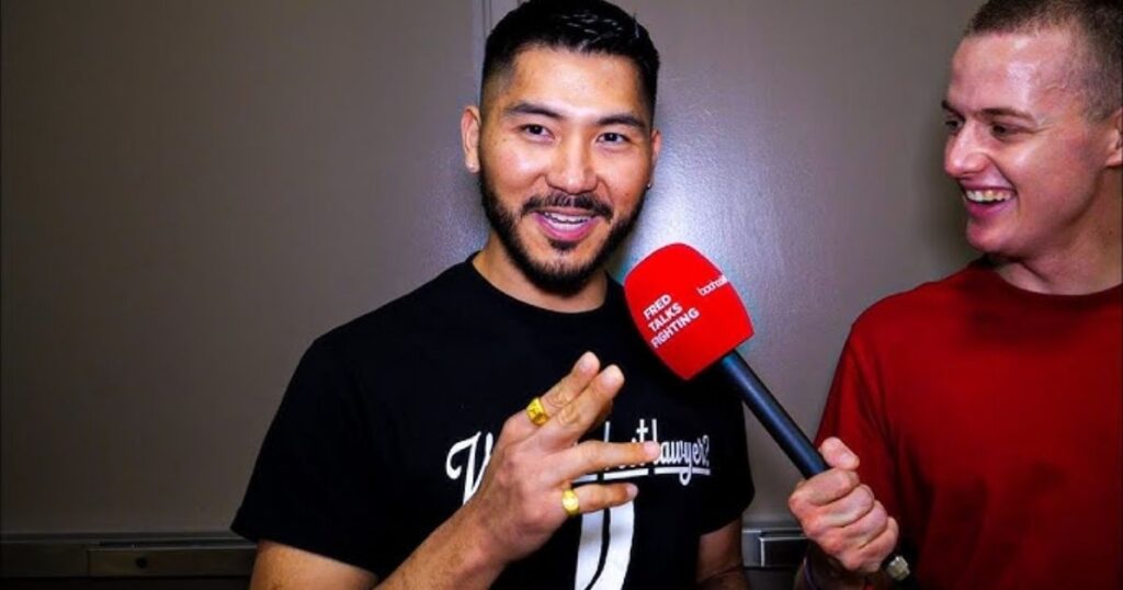 Two men with a microphone, one in a black shirt, the other in red.