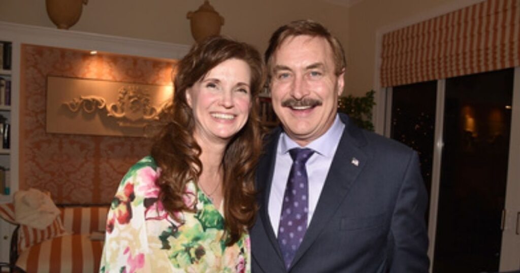 A man in a suit and a woman in a floral dress standing together in a room.