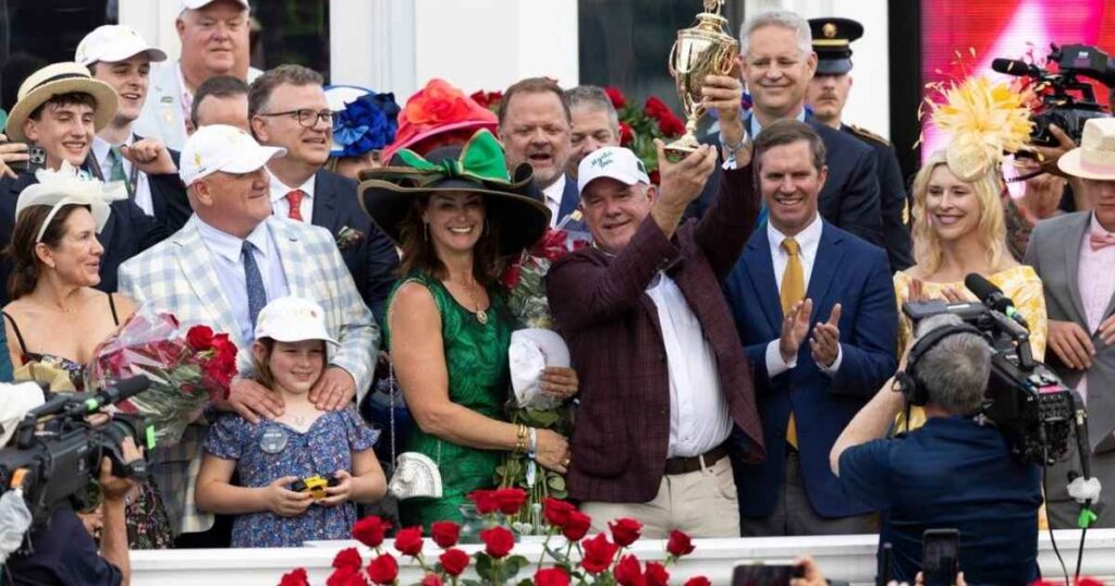 A group of elegantly dressed people with fancy hats celebrating at an event with a trophy and roses.